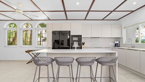 A modern kitchen with a central island, bar stools, and a ceiling fan.