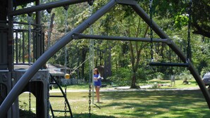 A playground with swings and a slide, surrounded by trees and grass.