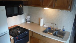 A compact kitchen with a stove, microwave, sink, and wooden cabinets.