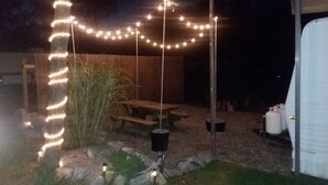 A backyard with a wooden deck, string lights, a picnic table, and a shed.