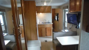 A compact RV interior with a kitchenette, seating area, and a television.