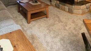 L’intérieur d’un chalet confortable, avec des murs en rondins de bois, une cheminée en pierre, un téléviseur à écran plat fixé au-dessus, une table basse en bois et un canapé d’angle gris.