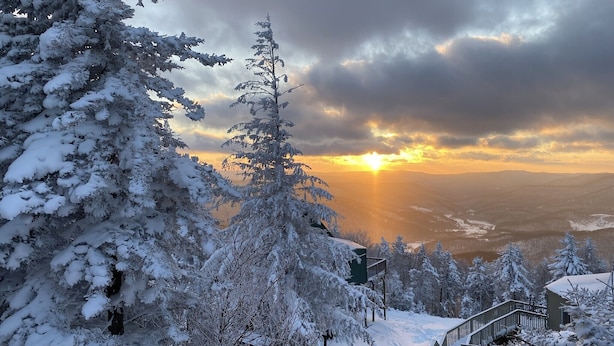 Un paysage enneigé avec une vue sur le coucher de soleil, un escalier en bois et un bâtiment doté d’un toit végétalisé.