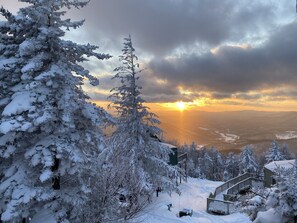 A snow-covered landscape with a sunset view, a wooden staircase, and a building with a green roof.