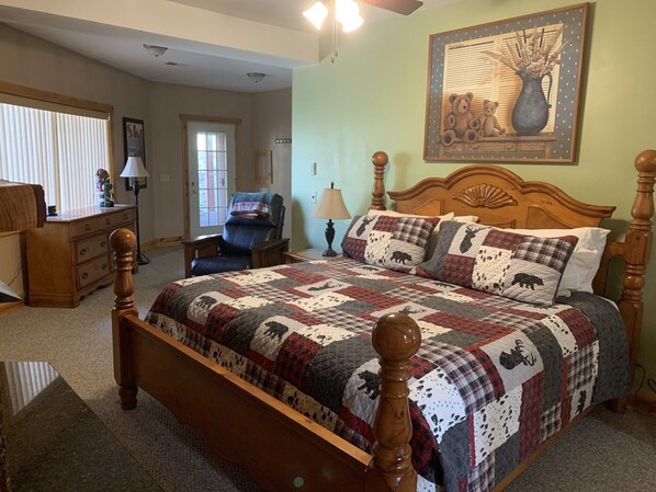 A bedroom with a large bed, a wooden headboard, a nightstand, a chair, a dresser, and a painting on the wall.
