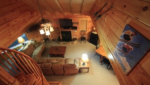 L’intérieur chaleureux d’un chalet, avec un décor en bois, une cheminée, un téléviseur et une affiche sur le thème du ski accrochée au mur.