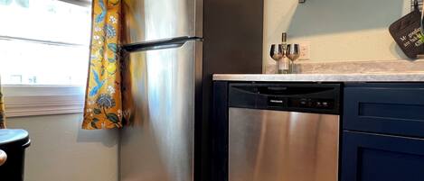 A kitchen with a stainless steel refrigerator, a dishwasher, and a window with curtains.