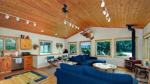 Un salón amplio con un sofá azul, techo de madera y ventanas grandes que ofrecen vistas al exterior.