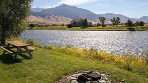Un área de picnic junto al lago con una fogata, una mesa de picnic y vistas a montañas al fondo.