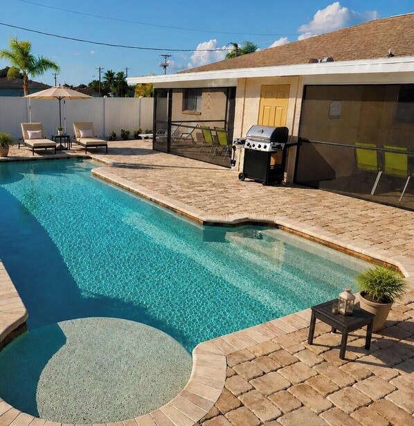 Ein Swimmingpool mit Liegestühlen, einem Grill und einer überdachten Terrasse.