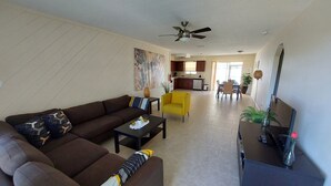 A living room with a sofa, a yellow armchair, a coffee table, and a TV on a stand.