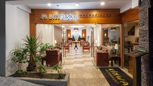 A hotel lobby with a reception desk, seating area, and a staircase leading to the upper floors. - Inti Punku Alameda Inn (Machu Picchu)