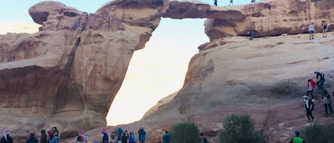 Un grupo de personas frente a una formación rocosa en arco bajo un cielo despejado.