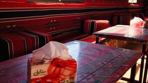 A room with striped red walls, a bench, and a table with a plastic bag on it. - camp Nights stars (Wadi Rum)
