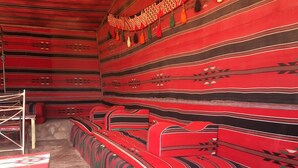 A room with a red patterned wall, a bench, and a table. - camp Nights stars (Wadi Rum)