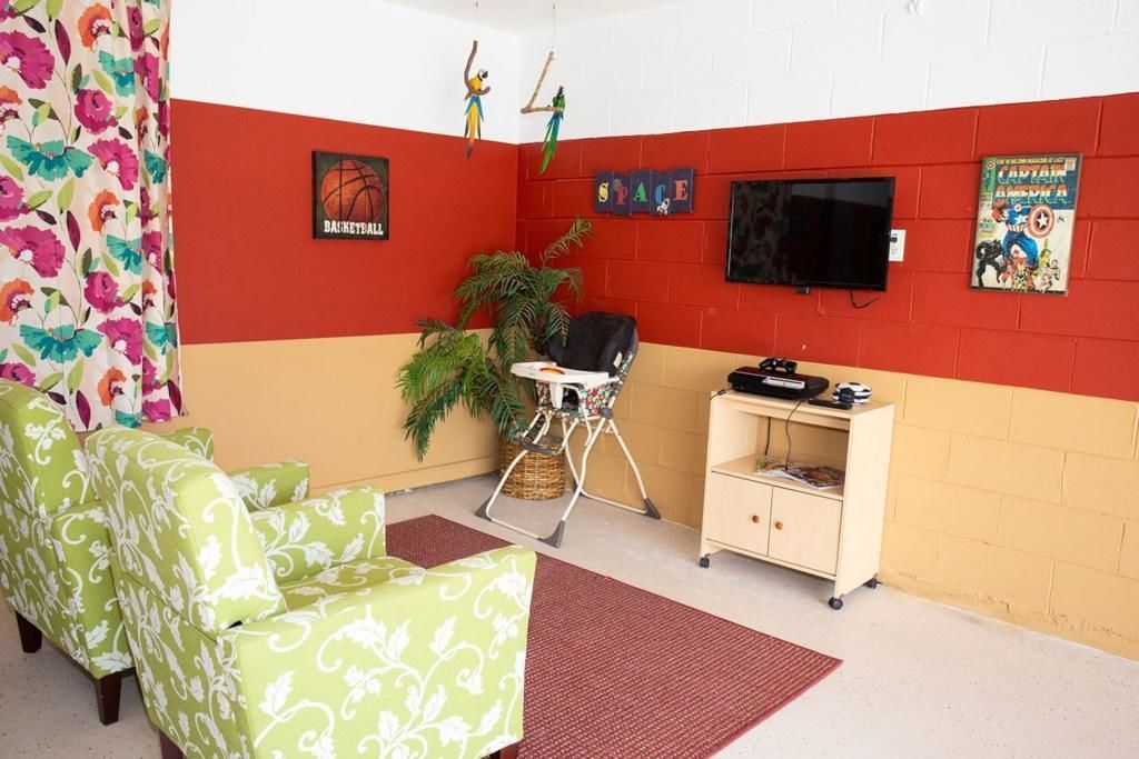 Una habitación con un sofá de color verde estampado, una mesita, un televisor y una estantería con objetos.