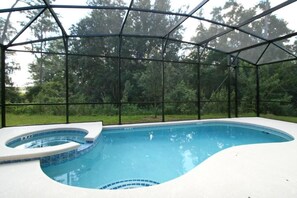Piscina com hidromassagem, cercada por um ambiente de vidro e árvores ao fundo.