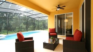 Un espacio de estar techado al aire libre con mobiliario de mimbre, piscina y puerta de cristal que da a un patio.