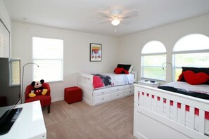 Quarto de criança com cama, escrivaninha, cadeira e ventilador de teto.