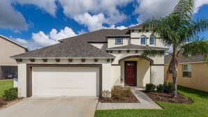 A two-story house with a garage, a red door, and a small garden with a palm tree.