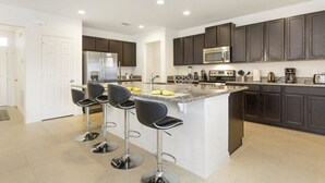 A modern kitchen with dark cabinets, a central island with bar stools, stainless steel appliances, and a white door.