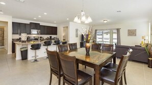A modern kitchen with dark cabinets, a central island with bar stools, and a dining area with a glass table and chairs.