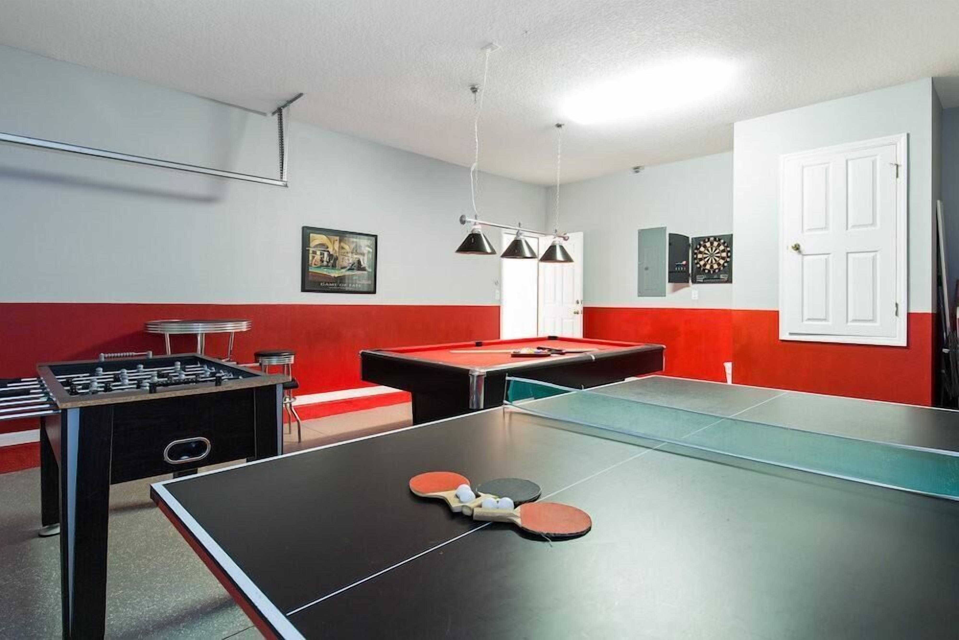 A room with a foosball table, ping pong table, and a dartboard.