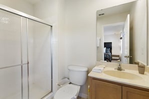 A bathroom with a glass shower enclosure, a toilet, a sink with a mirror, and a cabinet. - Villa Sonho - Encantada Resort (Kissimmee)