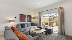 A modern living room with a grey sofa set, a coffee table, and a sliding glass door leading to a balcony. - Villa Magical - Encantada Resort (Kissimmee)