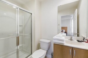 A bathroom with a glass shower enclosure, a white toilet, and a vanity with a mirror. - Villa Magical - Encantada Resort (Kissimmee)