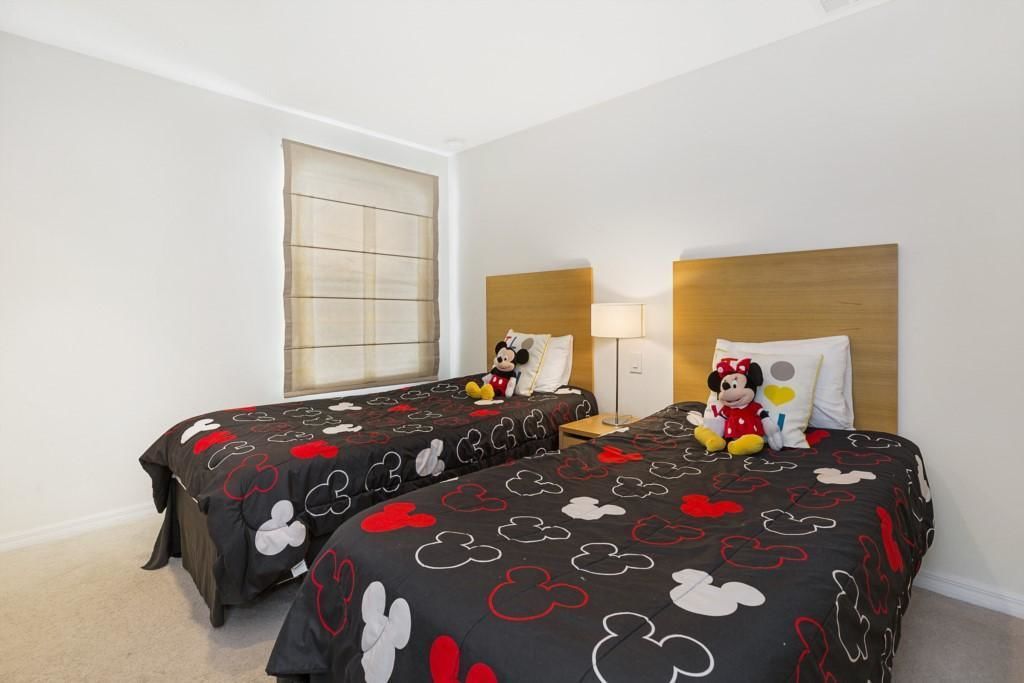 A hotel room with two beds, each with Mickey Mouse themed bedding. There is a nightstand with a lamp and a Mickey Mouse plush toy on one bed.
