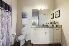 A bathroom with a toilet, sink, and mirror. There is a shower curtain with a wavy pattern. - Villa Cristina - Lucaya Village (Kissimmee)
