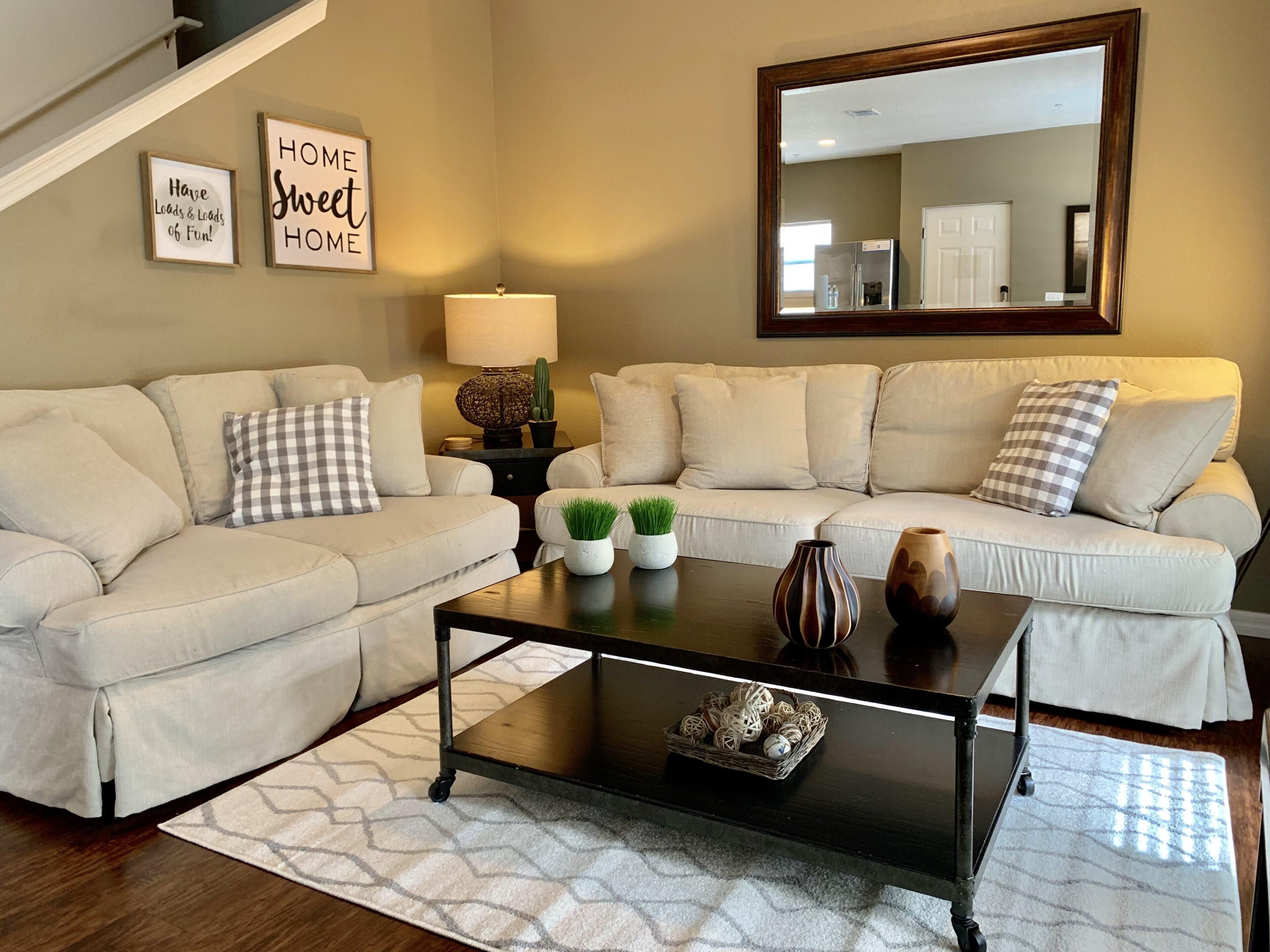A living room with two beige sofas, a coffee table, a lamp, and two wall-mounted signs.