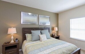 Une chambre à coucher avec un lit, deux tables de chevet, deux lampes et deux tableaux encadrés accrochés au mur.