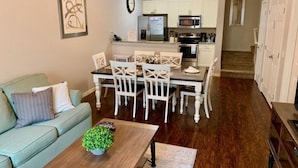 A modern living room with a dining area, a kitchen with white cabinets, and a staircase leading to another floor.