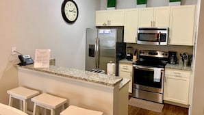 A compact kitchen with a built-in island, stainless steel appliances, and a clock on the wall.