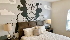 A bedroom with a bed, two nightstands, a wall mural, and a window.