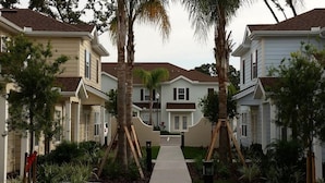 A residential street with houses, a central walkway, and palm trees.