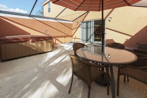 An outdoor patio with a round table and wicker chairs, a hot tub, and a glass door leading to a covered area.