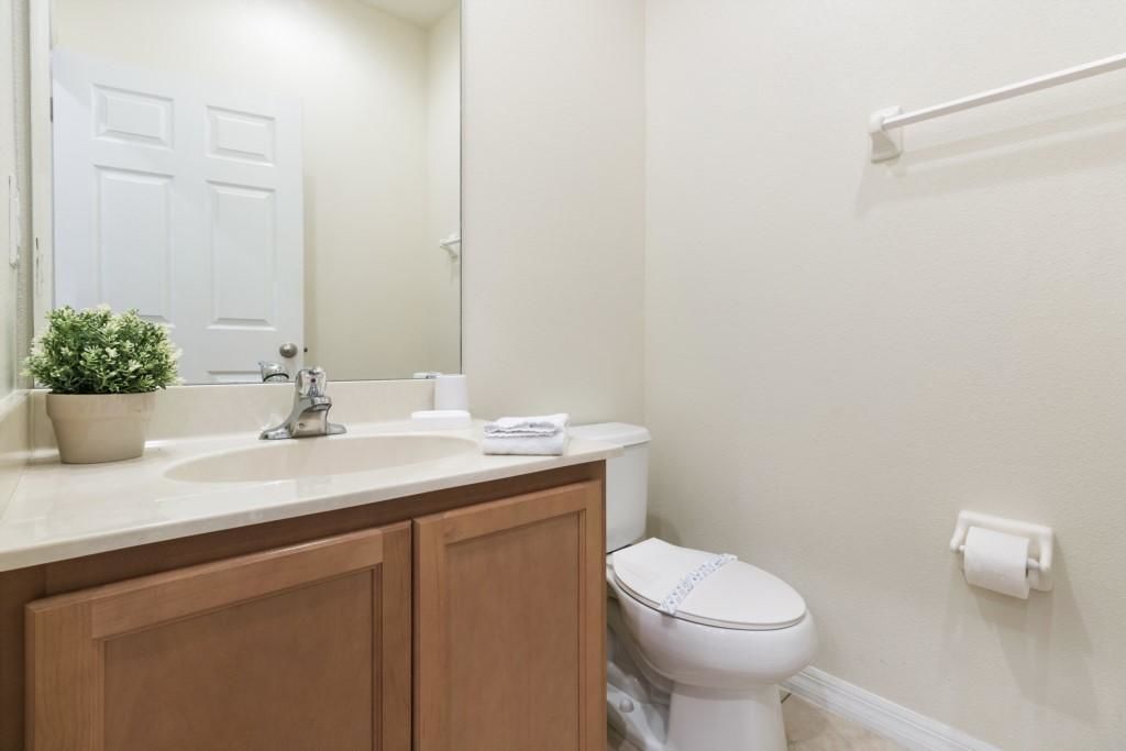 A bathroom with a white sink, wooden cabinets, a toilet, a mirror, and a potted plant.