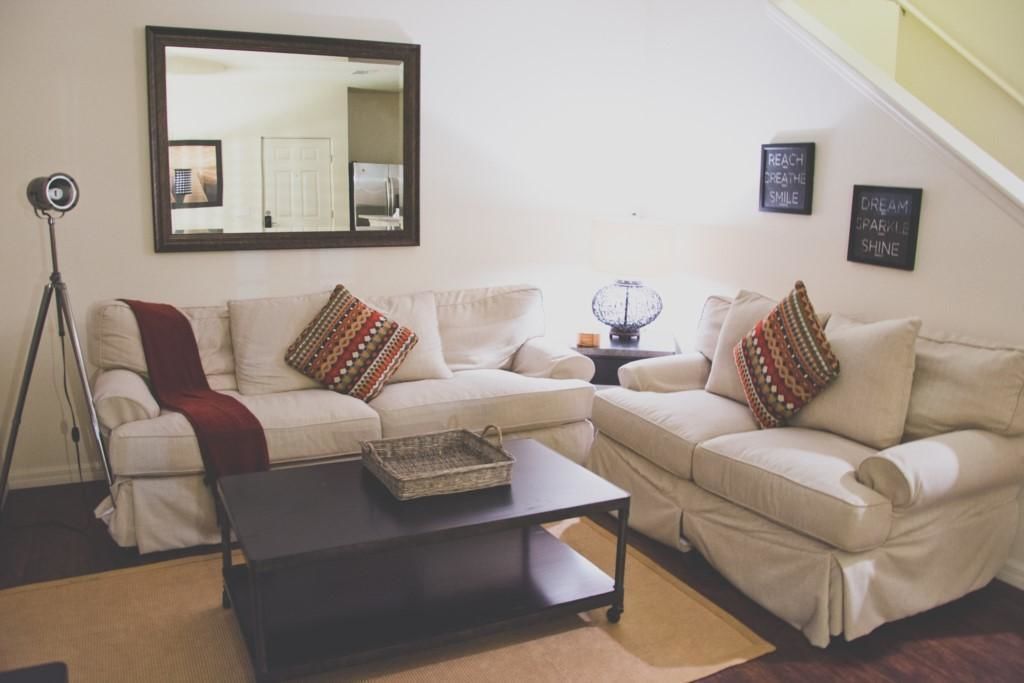 Una sala de estar con dos sofás color beige, una mesa baja oscura, una lámpara de pie y un espejo en la pared.