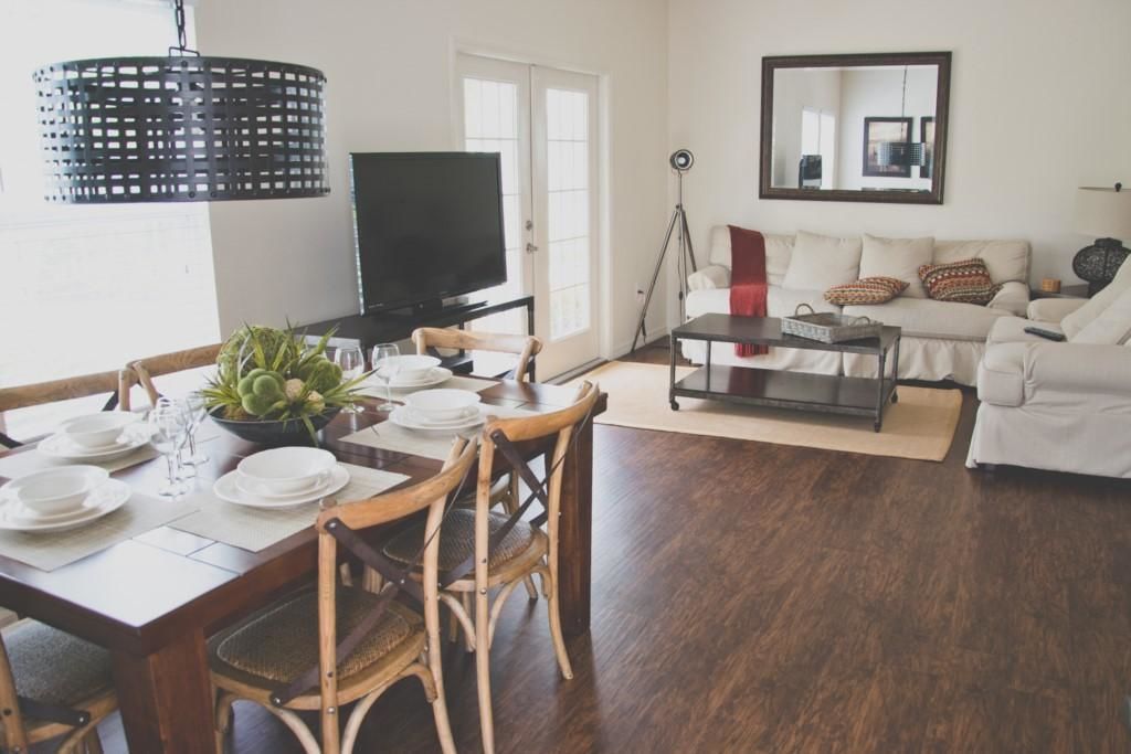 A dining area with a wooden table set for four, a television, and a sofa in the background.