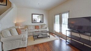 A living room with a sofa set, a coffee table, a TV on a stand, and a large window with blinds. - Villa Fonseca - Lucaya Village (Kissimmee)