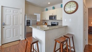 A kitchen with a central island, stainless steel appliances, and wooden stools. - Villa Fonseca - Lucaya Village (Kissimmee)