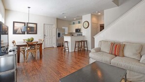 A spacious living room with hardwood flooring, a dining area with wooden chairs, a kitchen with a central island, and a staircase leading to another level. - Villa Fonseca - Lucaya Village (Kissimmee)