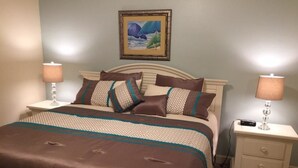 Ein ordentlich bezogenes Bett mit einer braunen und weißen Tagesdecke, zwei Nachttische mit Lampen und ein gerahmtes Bild an der Wand.