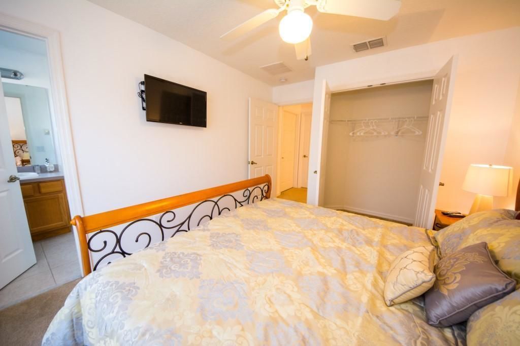 A bedroom with a bed, a television mounted on the wall, a ceiling fan, and a walk-in closet.