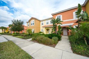 A row of townhouses with a central walkway, surrounded by lush greenery and palm trees.