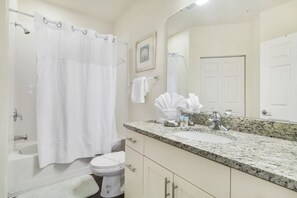 Un baño con bañera, inodoro, lavabo y un espejo grande.