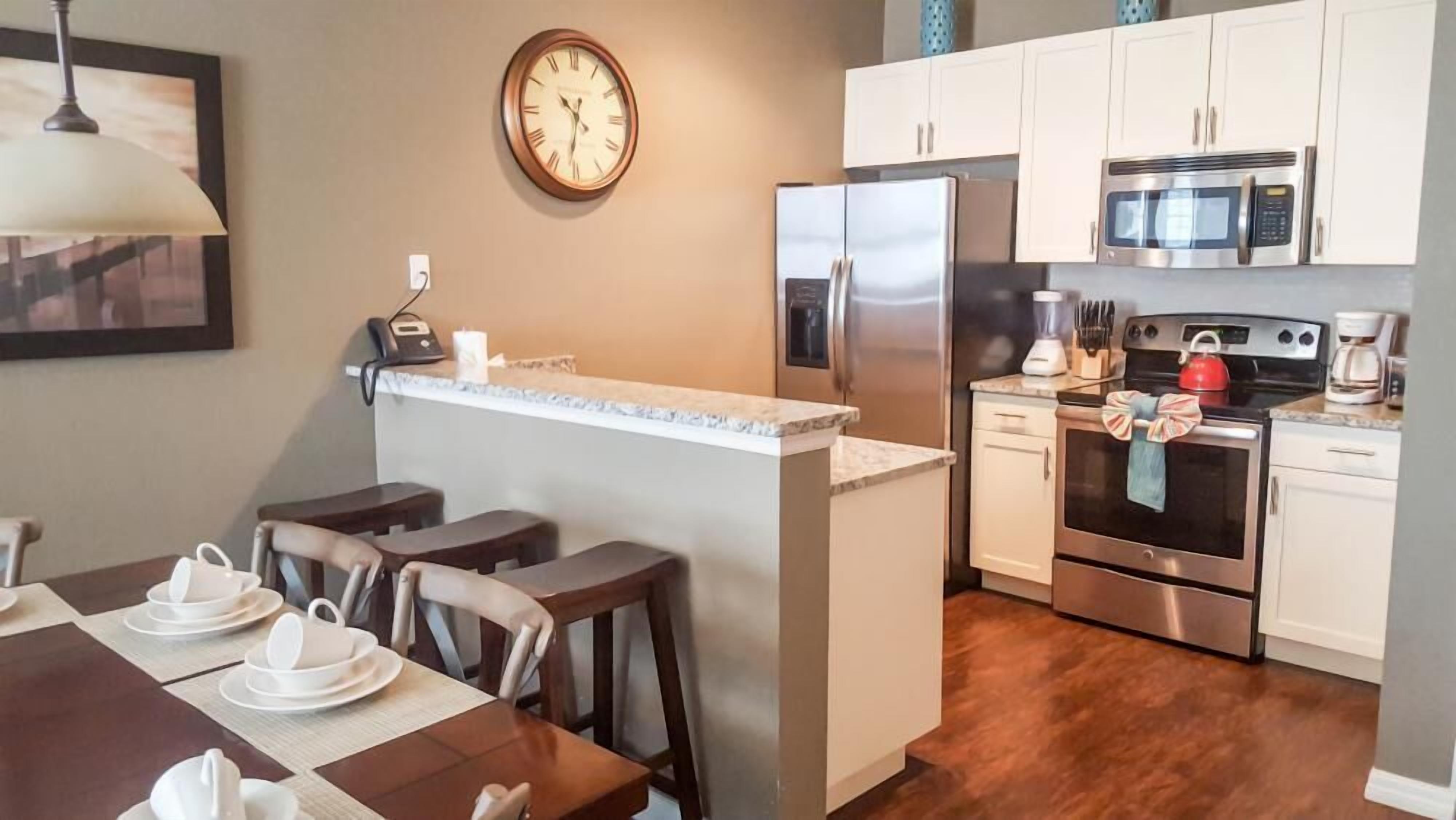 A compact kitchen with a refrigerator, microwave, stove, and a small island with stools.